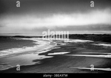 Una fotografia di paesaggio in bianco e nero cattura un'ampia e ampia spiaggia sotto un cielo spettacolare. La spiaggia si estende dal primo piano inferiore Foto Stock