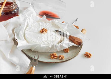 Formaggio brie fresco con noci e miele, servito con vino su tavola bianca. Vista frontale Foto Stock