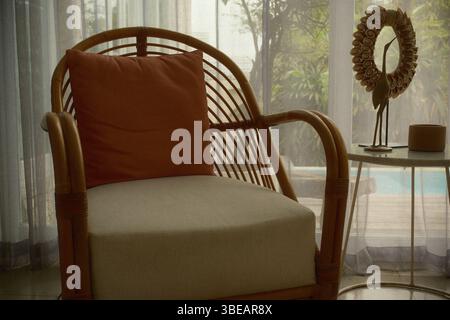 Angolo intimo con una poltrona in rattan, cuscino, un tavolino con piano in marmo bianco e una decorazione di sculture di uccelli a bordo piscina Foto Stock