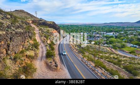 Tortuosa strada di montagna aerea con auto bianca e passaggio da città deserta Foto Stock