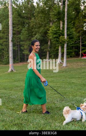 Una donna con un vestito verde cammina i suoi due cani in un parco. Sta sorridendo e sembra che si stia godendo il suo tempo con i suoi animali domestici Foto Stock