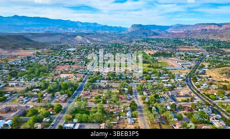 I quartieri aerei della piccola città con le Red Rock Mountains e gli alberi verdi volano sopra Foto Stock