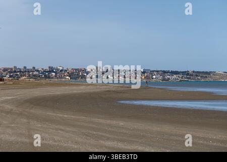 Buzovna, Azerbaigian. Una tranquilla scena urbana costiera caratterizzata da una vasta spiaggia di sabbia, una costa calma e cieli azzurri che catturano la bellezza serena Foto Stock