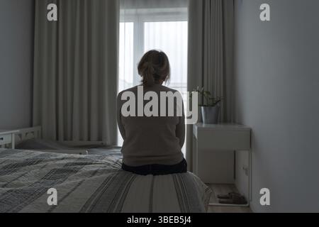 Donna matura seduta da sola nella stanza, triste persona depressa. Vista posteriore. salute mentale che problemano la popolazione. Foto Stock