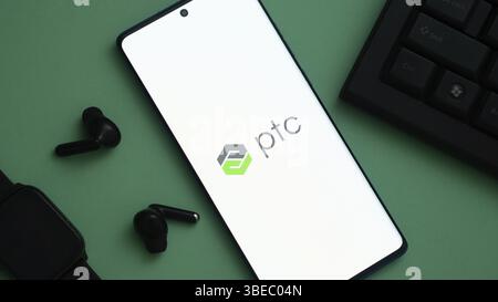 Smartphone con logo ptc, circondato da accessori tecnologici su una superficie verde Foto Stock