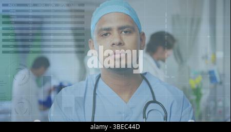 Medico in piedi in scrub blu e cappuccio che tiene lo stetoscopio nel reparto, con monitor che regolano il team Foto Stock