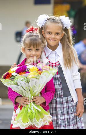 Ritratto di due ragazze nella scuola 1 settembre - il primo-grader e la sua sorella più giovane con un mazzo di fiori in mani Foto Stock