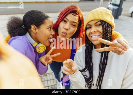 Tre studenti latini, che si divertono insieme in una giornata di sole, mostrano segni di pace ed espressioni allegre Foto Stock