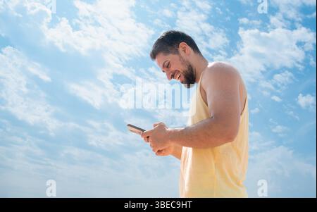 Ridendo lo spagnolo giovane sulla spiaggia scrivendo messaggi con il cellulare e un bel cielo azzurro Foto Stock