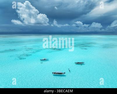 Vista aerea di barche e yacht colorati in acque cristalline in estate. Isola di Mnemba, Zanzibar. Vista dall'alto del banco di sabbia con la bassa marea, il mare blu e le persone che nuotano Foto Stock