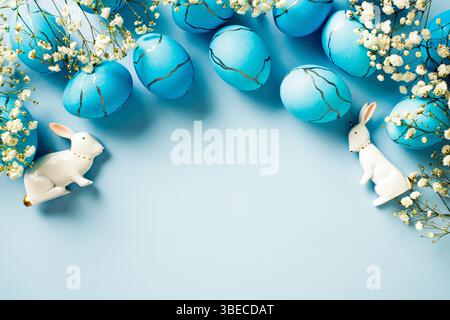 Uova di Pasqua blu, fiori, conigli su sfondo blu. Disposizione piatta, vista dall'alto, spazio di copia. Foto Stock
