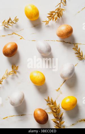 Buona Pasqua composizione piatta. Uova di Pasqua e foglie dorate sul tavolo in marmo. Foto Stock