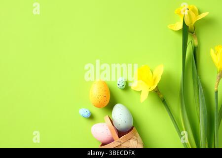 Cestino con uova di Pasqua colorate e fiori di narcisi sul green table. Design banner per buona Pasqua. Foto Stock