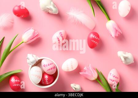 Buona composizione pasquale. Uova di Pasqua colorate, tulipani, coniglietti decorativi su sfondo rosa. Disposizione piatta, vista dall'alto. Foto Stock