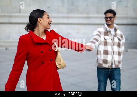 Giovane coppia multietnica che si tiene per mano e cammina in un ambiente urbano, godendosi una romantica passeggiata insieme Foto Stock