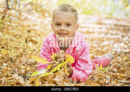 6 anno vecchia ragazza giacente sul giallo foglie caduti nel giorno di autunno caldo nei boschi Foto Stock