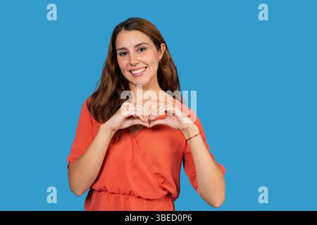 Ritratto in studio di una allegra donna d'affari che mostra il segno del cuore con le mani, esprimendo amore e cura Foto Stock