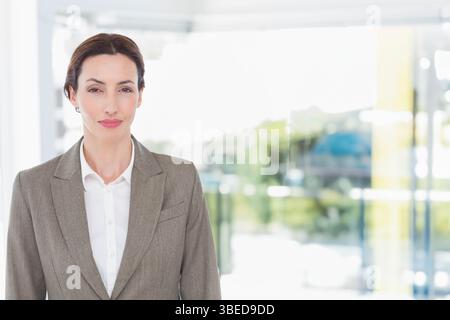 Donna adulta che indossa un blazer grigio in piedi nella hall dell'ufficio vicino a pannelli di vetro che rivelano il verde Foto Stock