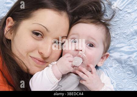 Mamma e sei mesi di figlia felicemente distesi sul lettino Foto Stock