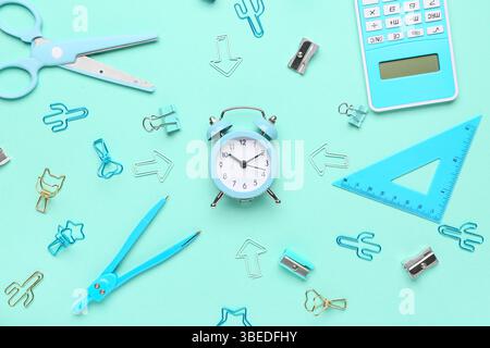 Composizione con sveglia e cancelleria scolastica diversa su sfondo turchese Foto Stock