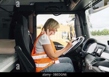 Donna matura, conducente di camion, volante all'interno della cabina dell'autocarro. Felice ritratto di camionista di mezza età . Foto Stock