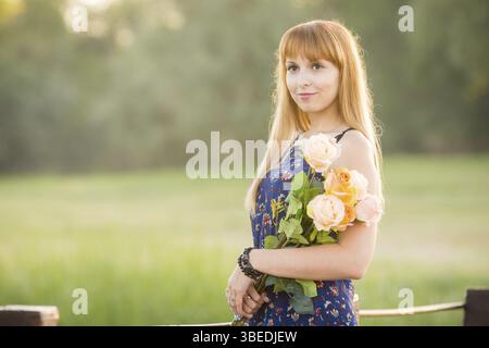 Bella ragazza in piedi su un ponte sul fiume con un bouquet di fiori. Ritratto Foto Stock