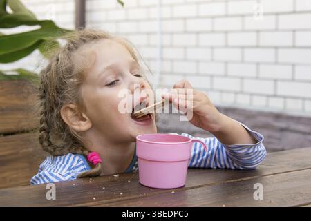 Quattro anni di ragazza cialde per mangiare e bere il tè al tavolo sulla veranda Foto Stock