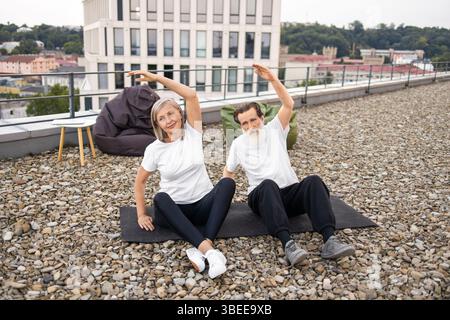 Coppie più anziane che praticano yoga insieme all'aperto su una terrazza sul tetto Foto Stock