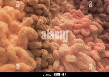La mano di una donna tocca il morbido filato di peluche in colori caldi e accoglienti. Filati colorati. Negozio di artigianato. Uncinetto e maglia. Immagine opaca. Comfort di casa. Foto Stock