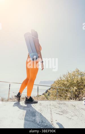 Donna in Orange Leggings che porta un tappetino da yoga Foto Stock
