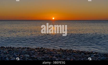 Tramonto dorato sulla tranquilla Pebble Beach e sulle dolci onde dell'Oceano Foto Stock