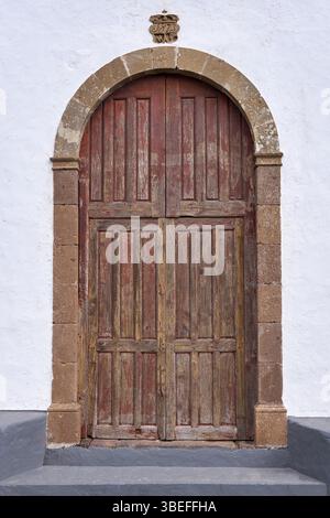 Vecchia porta marrone della chiesa in legno in un portale rotondo in pietra Foto Stock