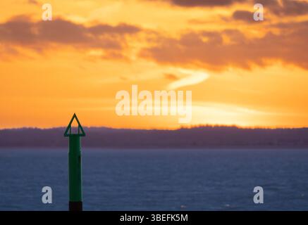 Palo di navigazione verde sagomato contro un cielo arancione al tramonto vicino all'Isola di Wight, Inghilterra. Uso editoriale solo per la qualità. Foto Stock