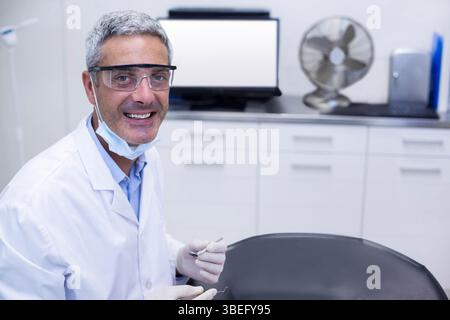 Dentista maschio che indossa un camice da laboratorio e occhiali di protezione che tengono lo specchio e la sonda dentale in funzione, spazio di copia Foto Stock