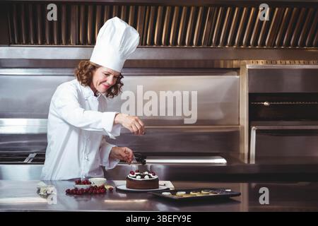 Torta al cioccolato ricoperta di ciliegie sul banco in acciaio nella cucina professionale, con pasticcini Foto Stock