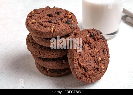 Pila di biscotti con scaglie di cioccolato e un bicchiere di latte. Biscotti al cioccolato fondente fatti in casa con nocciole. Foto Stock
