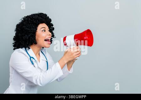 Medico donna che parla con gioia attraverso un megafono, indossa un cappotto bianco e uno stetoscopio Foto Stock