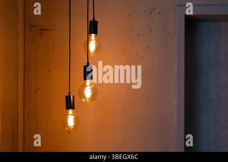Tre lampade decorative sospese dal soffitto emettono una calda luce soffusa contro una parete testurizzata. Le luci migliorano l'atmosfera accogliente e. Foto Stock