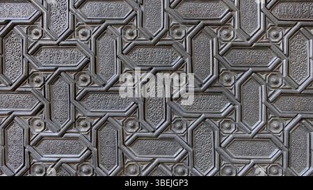Decorato motivo geometrico islamico scolpito su una superficie in metallo che mostra intricate lavorazioni artigianali e dettagliate iscrizioni calligrafiche, design ripetuto Foto Stock