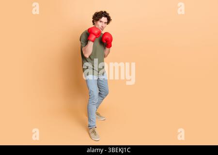 Giovane con un abbigliamento casual che indossa guanti da boxe rossi in posa difensiva di fronte a uno sfondo beige Foto Stock