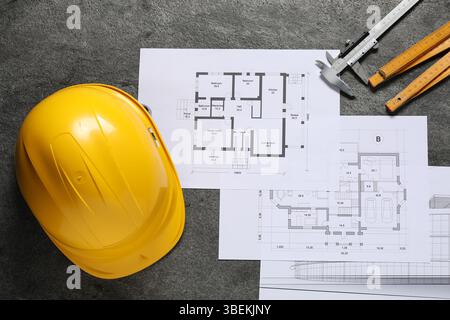 Diversi disegni architettonici, elmetto, righello pieghevole e calibro a corsoio su tavolo grigio, disposizione piatta Foto Stock