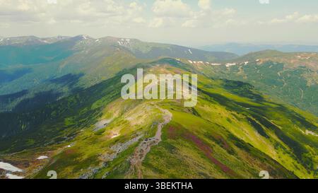 Vista aerea di una lussureggiante catena montuosa con sentieri escursionistici. Una splendida vista aerea di una vibrante catena montuosa, coperta da vegetazione verde con visibile Foto Stock