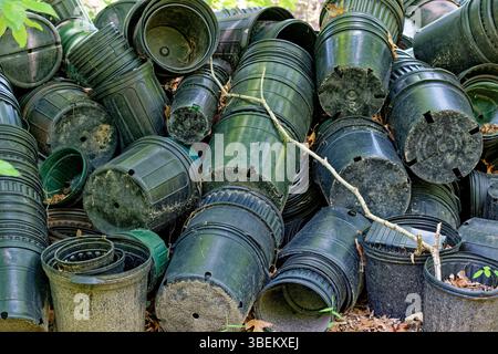 Svuotare grandi e piccoli contenitori di piante da giardino in plastica verde e nera sporchi o vasi impilati insieme gettati in un mucchio di vista ravvicinata del terreno Foto Stock