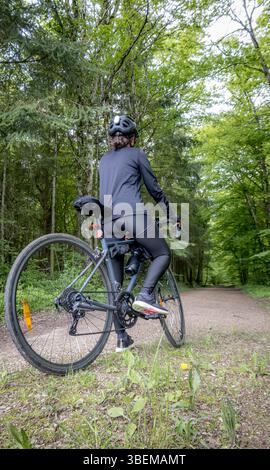 Il ciclista che indossa abiti neri e casco corre in bicicletta su un sentiero nella foresta in primavera. Circondato da una vegetazione lussureggiante, la scena cattura l'avventura all'aperto Foto Stock