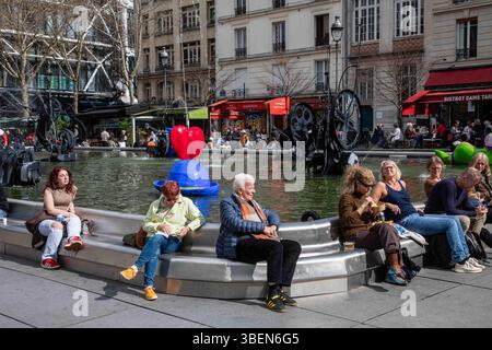 Persone che si rilassano presso la Fontana Stravinsky in Place Igor Stravinsky in una giornata di sole nel quartiere Marais di Parigi, Francia Foto Stock