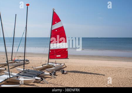 Un catamarano su una spiaggia sabbiosa in Bretagna, con la sua vela rossa e bianca Foto Stock