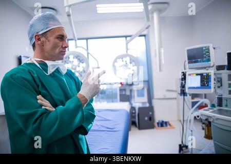 Chirurgo maschile in piedi accanto al tavolo operatorio in sala operatoria che controlla il monitor paziente e lo spazio di copia Foto Stock