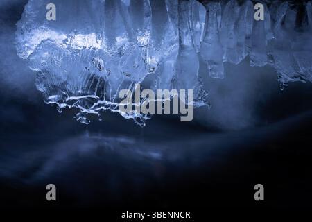 Formazioni di ghiaccio scultoree si stendono sopra un flusso di acqua scura e in movimento, illuminate da fresche tonalità blu. Foto Stock