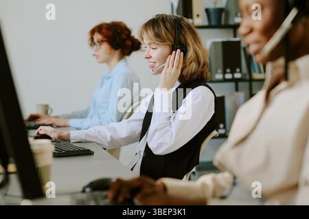 Gruppo di diversi operatori di contact centre che lavorano con cuffie e auricolari, impegnati in attività di assistenza clienti. Team multietnico che si concentra sulle chiamate e fornisce assistenza Foto Stock