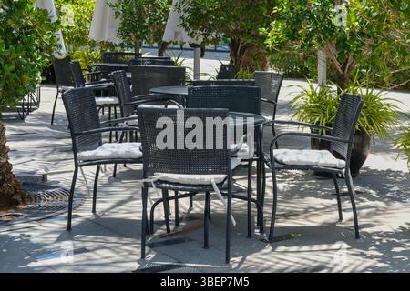 Accogliente area all'aperto con posti a sedere di un ristorante vuoto o di un bistrot circondato da piante su vasi di fiori. Tavoli e sedie neri con cuscini sul patio o sui caffè. Foto Stock